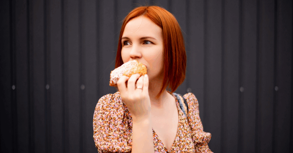 A woman eating a pastry and looking off to the left