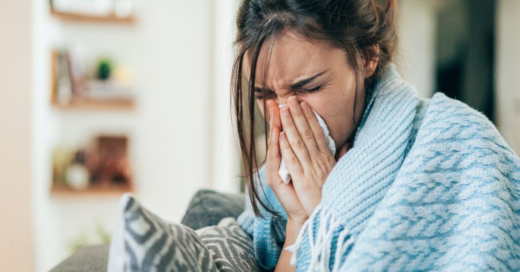 A woman wrapped in a blue blanket and sneezing into a tissue